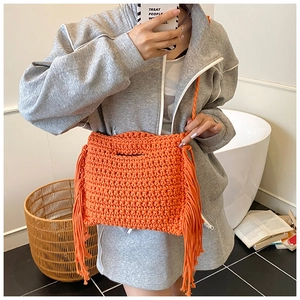 Detail of vibrant orange hand-knitted shoulder bag featuring long fringe side accents