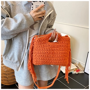 Detail of orange hand-knitted crossbody bag featuring vibrant side fringe and texture