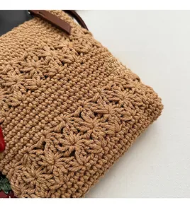 Detail des handgewebten Blumenmusters und des braunen Lederriemens einer Strohtasche