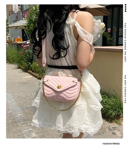 Outdoor shot of a pink quilted shoulder bag with gold chain strap on white dress