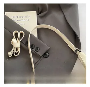 Detail of cream leather shoulder strap with silver metal buckles on a grey blazer