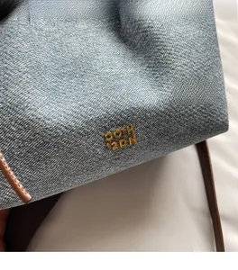 Dettaglio della trama in denim azzurro e del logo in metallo dorato sulla borsa a tracolla