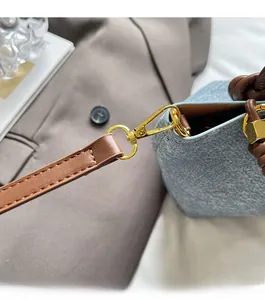 Dettaglio della fibbia dorata e tracolla in pelle marrone su borsa blu testurizzata