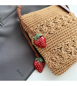 Detail der khakifarbenen gewebten Tasche mit Blumenmuster und roten Erdbeer-Anhängern