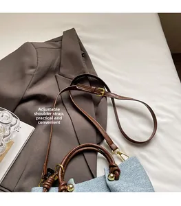 Dettaglio tracolla regolabile in pelle e manico intrecciato su borsa in denim