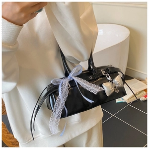 Détail du sac en cuir verni noir avec nœud en dentelle blanche et pendentif argenté