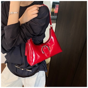 Detail of a vibrant red patent leather underarm bag with a shiny silver round buckle strap