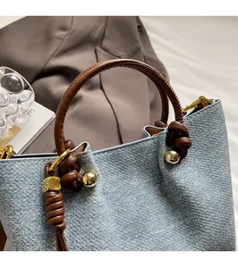 Dettaglio borsa in denim blu con manico in pelle marrone e inserti in metallo dorato