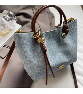 Dettaglio borsa a secchiello in denim azzurro con manico in pelle marrone e hardware oro