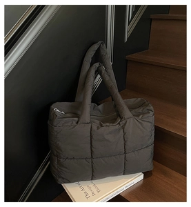 Detail shot of a dark grey quilted puffer tote bag with a soft padded handle on steps
