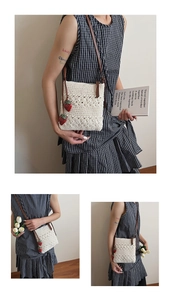 Close-up of white crochet bucket bag with red strawberry charm and leather strap