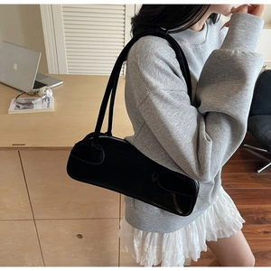 Detail shot of a minimalist black leather baguette bag on model with modern office background