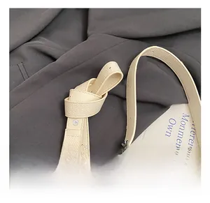 Macro detail of beige pebble leather shoulder strap with a knotted adjustable design