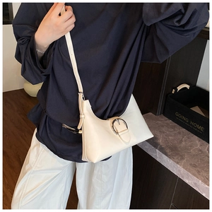Detail of a beige crescent underarm bag featuring a large silver circular metal buckle accent