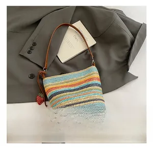 Detail of a rainbow woven straw bag featuring leather straps and red strawberry charms