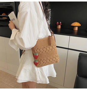 Detail of woven crossbody bag featuring textured floral patterns and strawberry charms