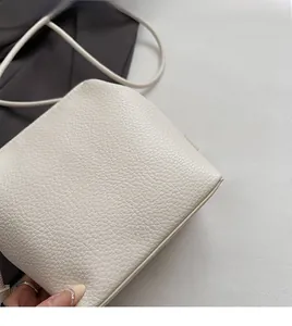 Detailed macro view of the cream-white pebbled leather texture on this minimalist shoulder bag