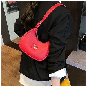 Detail of red crescent shoulder bag with lychee texture and metallic logo on black outfit