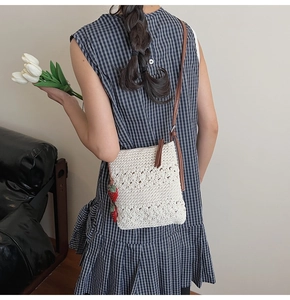 Detail of white crochet crossbody bag with floral patterns and strawberry charm accessory
