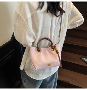 Dettaglio della borsa rosa chiaro con manici in pelle marrone e logo in metallo oro