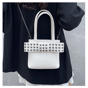Side view of white studded crossbody bag with bow detail on a model in a black blazer