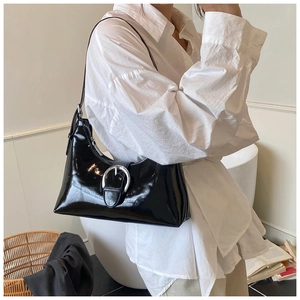 Detail shot of black glossy underarm bag with a large silver metal buckle on white shirt