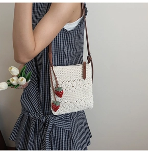 Detail of woven straw shoulder bag with cute strawberry charms and brown leather strap