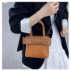 Détail d'un sac à main marron avec texture litchi, rivets argentés et bandoulière chaîne