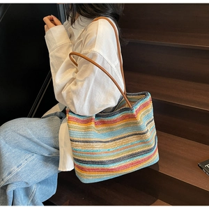 Detail of colorful woven rainbow tote bag featuring vertical stripes and brown handles