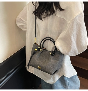 Foto lifestyle di una borsa a secchiello grigia con manici neri e dettagli oro