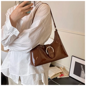 Brown patent leather underarm bag with large silver buckle shown on shoulder