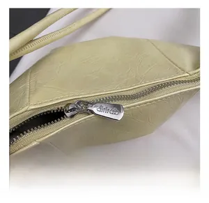 Close-up of silver metal zipper with dirirab engraving on a beige pleated handbag