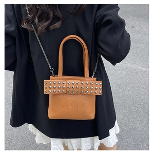 Brown punk rivet chain bag with bow detail worn as a crossbody by a model in a suit