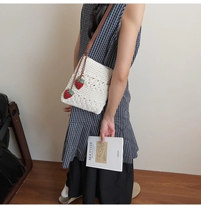 Detail of white crochet crossbody bag with red strawberry charms and leather strap
