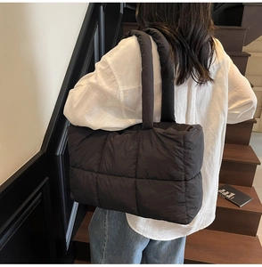 Close-up of oversized black quilted tote bag worn over the shoulder by a model