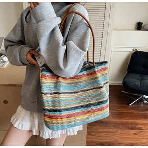 Close-up of a colorful woven tote bag with leather handles shown on a model