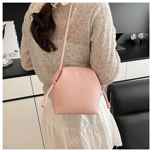 Detail of pink pebbled leather bucket bag with side drawstring knot shown on model