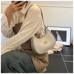 Detail of silver crescent hobo bag featuring grain texture and metallic logo plaque
