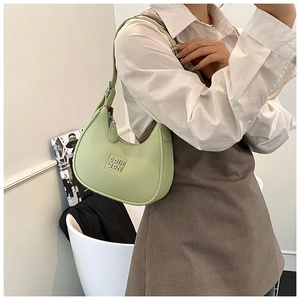 Close-up of a light green crescent-shaped underarm bag with litchi texture on model