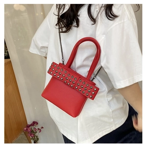 Detail of red pebbled leather handbag featuring rivet bow and metallic chain strap