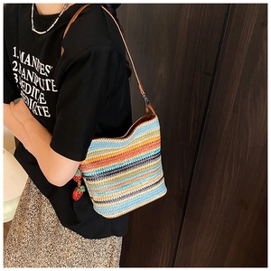 Detail of colorful striped woven bucket bag featuring red strawberry charms and leather strap