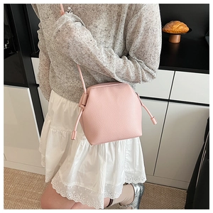 Gros plan d'un sac bandoulière rose à cordon en cuir texturé litchi porté par un mannequin