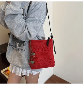 Close-up of handmade red crochet crossbody bag with strawberry charms and floral knit