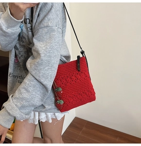 Detail of red hand-woven crochet bag featuring cute 3D strawberry charms and black strap