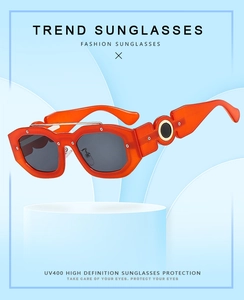 Detail of orange square sunglasses with UV400 lenses and metal hinge studs on blue stand