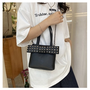Détail du sac en cuir noir à rivets avec bandoulière chaîne porté par un mannequin