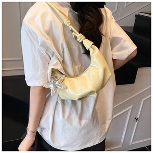 Detail of cream pleated crescent bag with a decorative silver star and woven strap