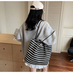 Close-up of black and white striped woven tote bag with slim shoulder straps on a person