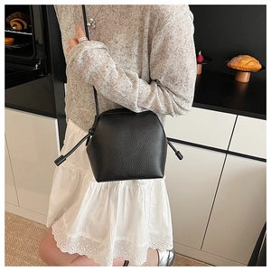 Detail of a black pebbled leather crossbody bag with drawstring design shown on a model