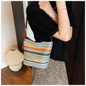Close-up of rainbow striped straw shoulder bag with brown leather strap and red tassel
